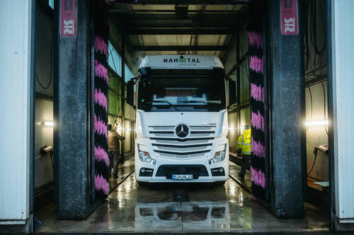 Ein LKW mit der Aufschrift „Nahetal-Logistik“ fährt durch eine Waschanlage. Rechts und links sind pink-schwarze Bürsten zu sehen.